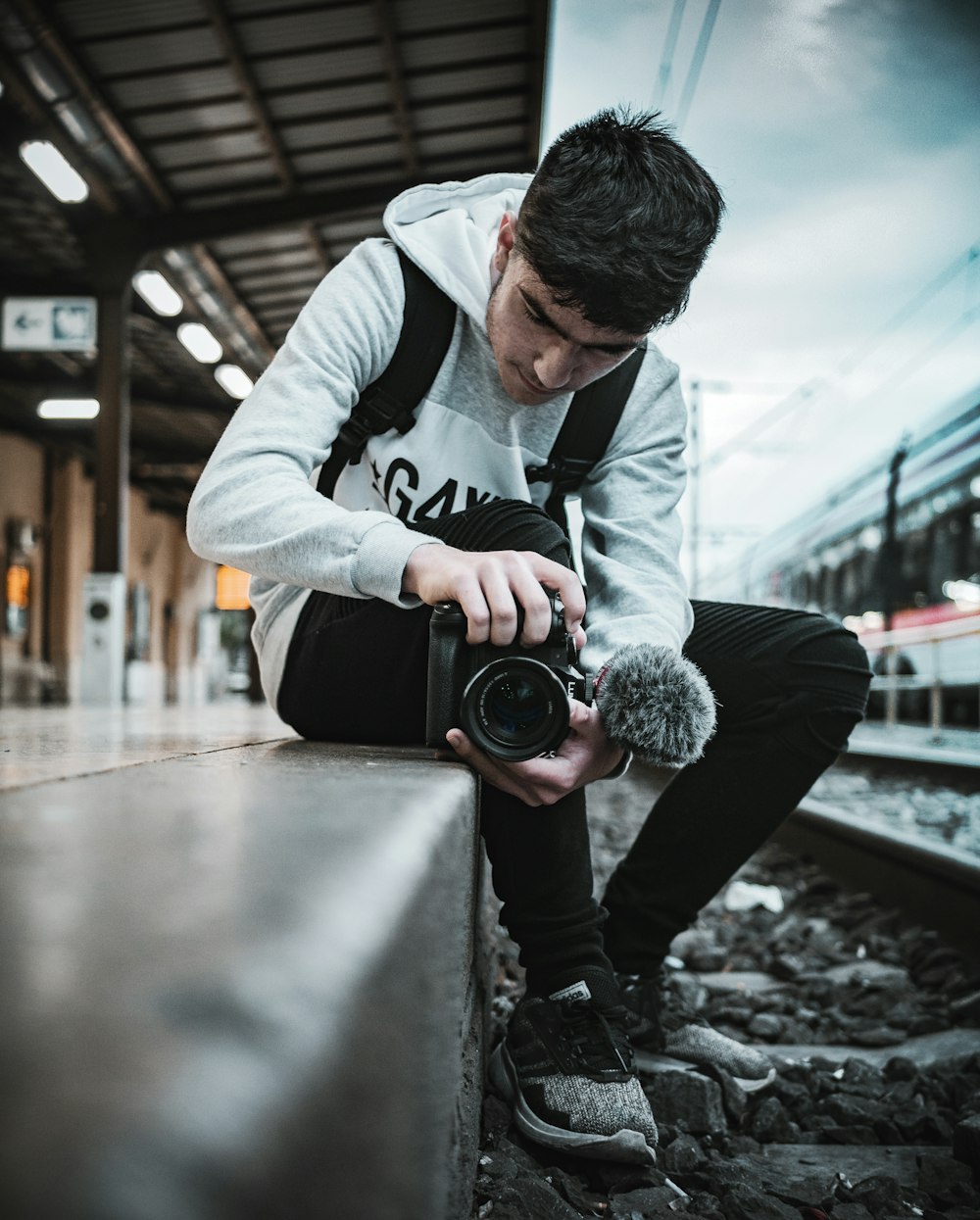 man sitting beside rail track holding camera