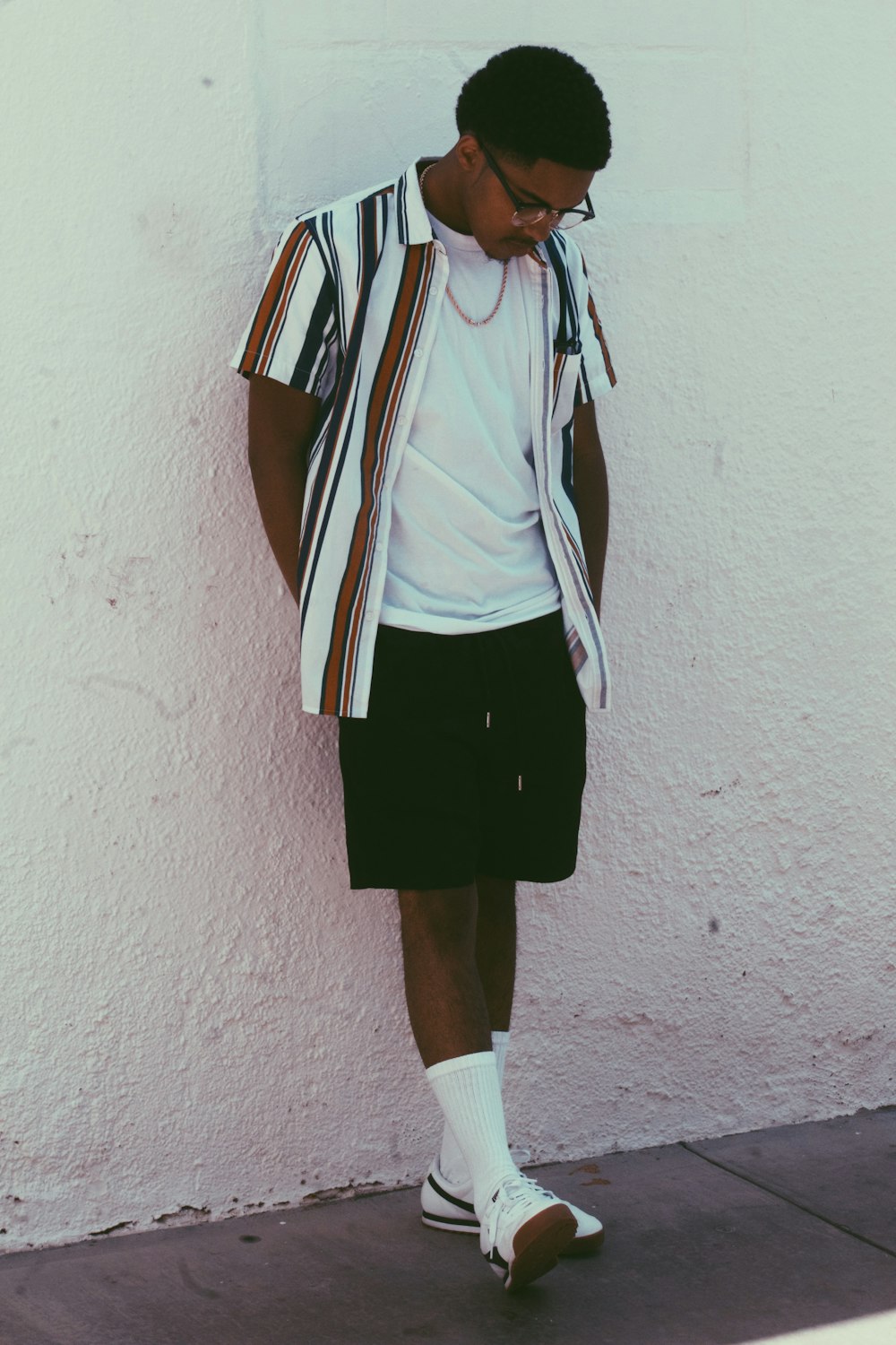 man wearing white, black, and brown shirt leaning on white wall