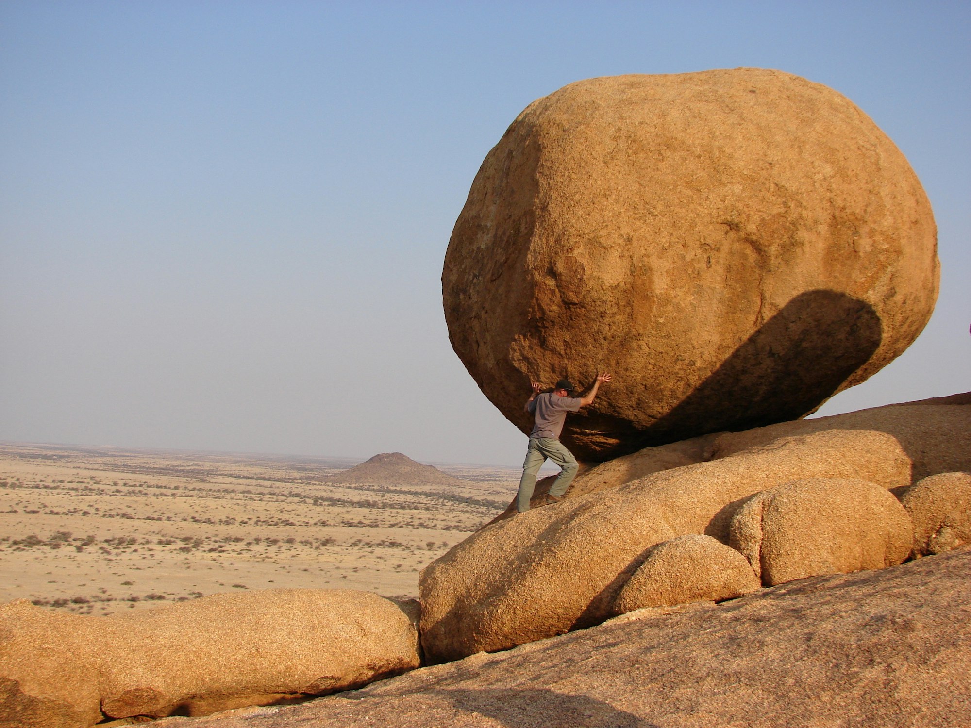 A person pretends to be pushing a boulder several times larger than him up a hill.