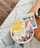 A person holding a healthy smoothie bowl with fresh fruits and seeds on a wooden table.