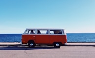 Modern utilitarian van parked against a backdrop of vibrant orange sunshine over seaside cliffs.