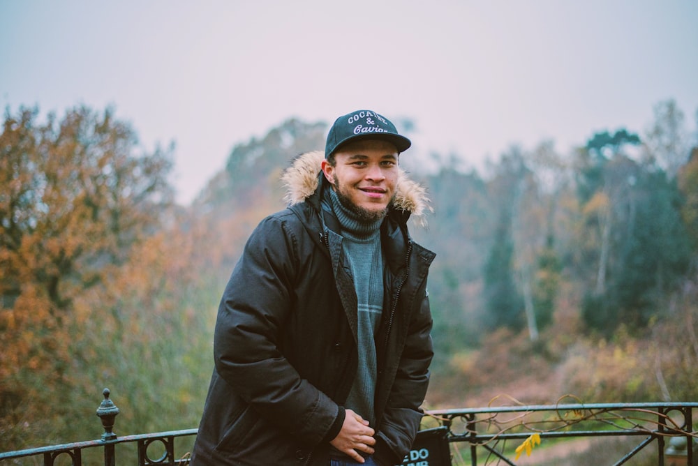 smiling man wearing parka in front of handrail and trees