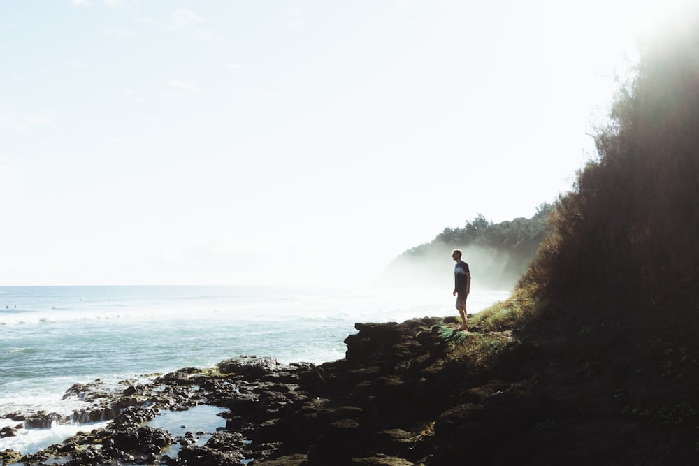 man standing on rocky hill looking on sea