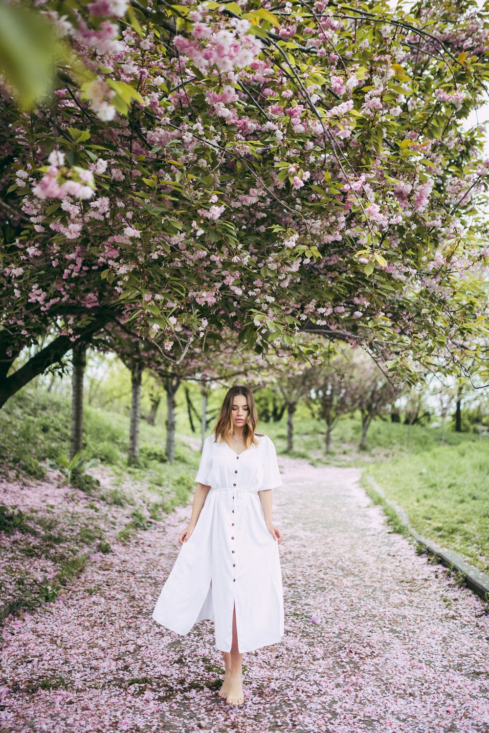 woman in white dress standing on trail under cherry blossom tree