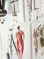 Celia Martins discussing fashion sketches with a client in a cozy studio.