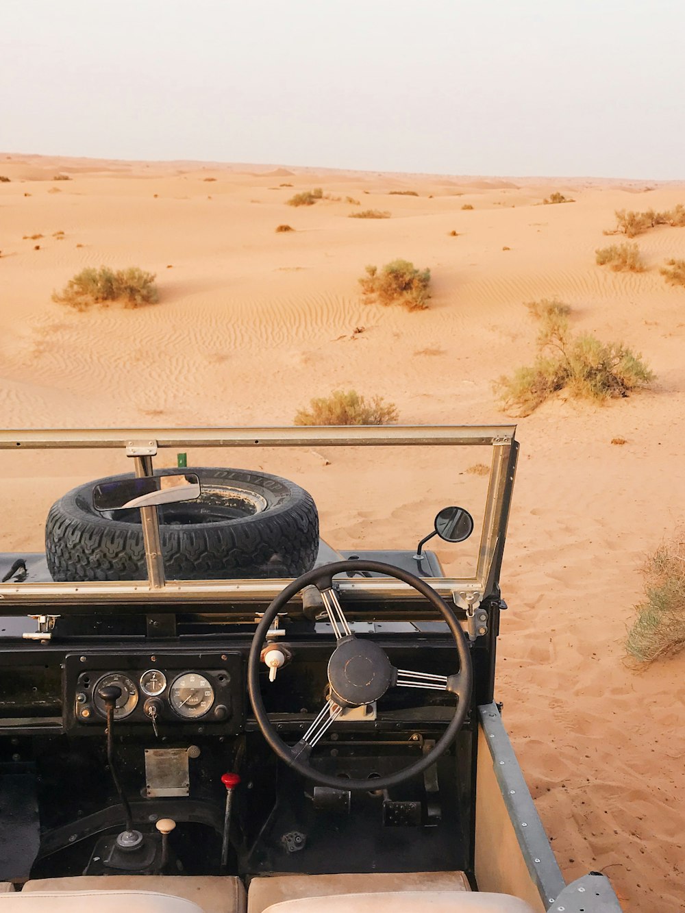 grey Land Rover Defender with top down parked at the desert