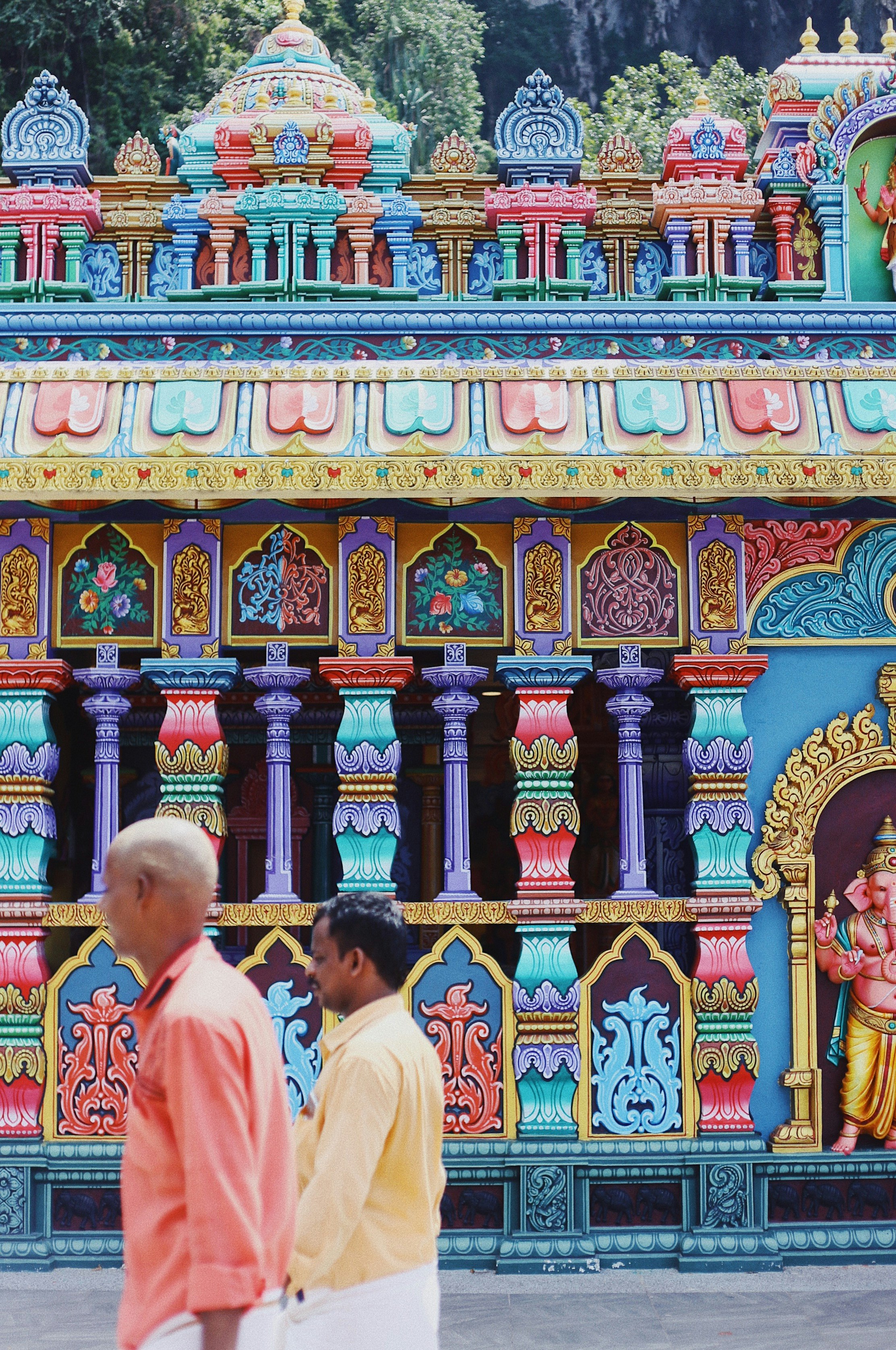 two men walking in front of multicolored building with Ganesha statue
