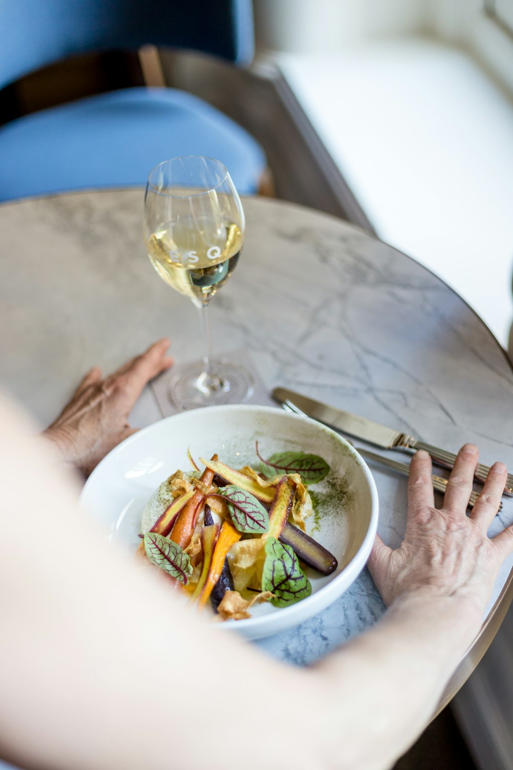 person by the round table with salad meal and white wine