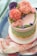 A beautifully decorated cake featuring intricate buttercream flowers in shades of pink, purple, peach, and green. The cake has a green patterned layer with yellow accents, all placed on a blue and pink tray with a floral cloth beneath it.