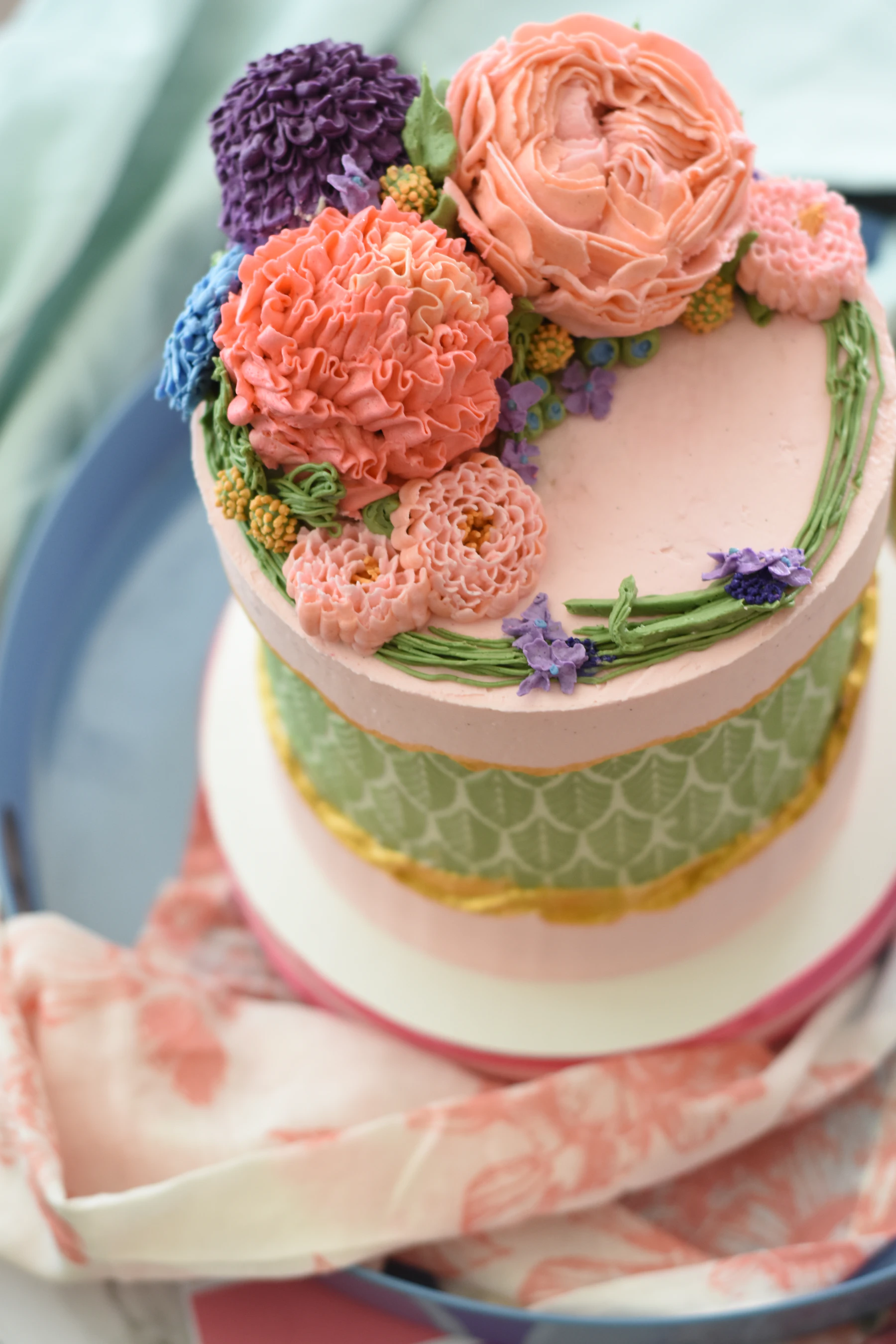 A pink layer cake topped with piped buttercream peony, carnation and chrysanthemum flowers