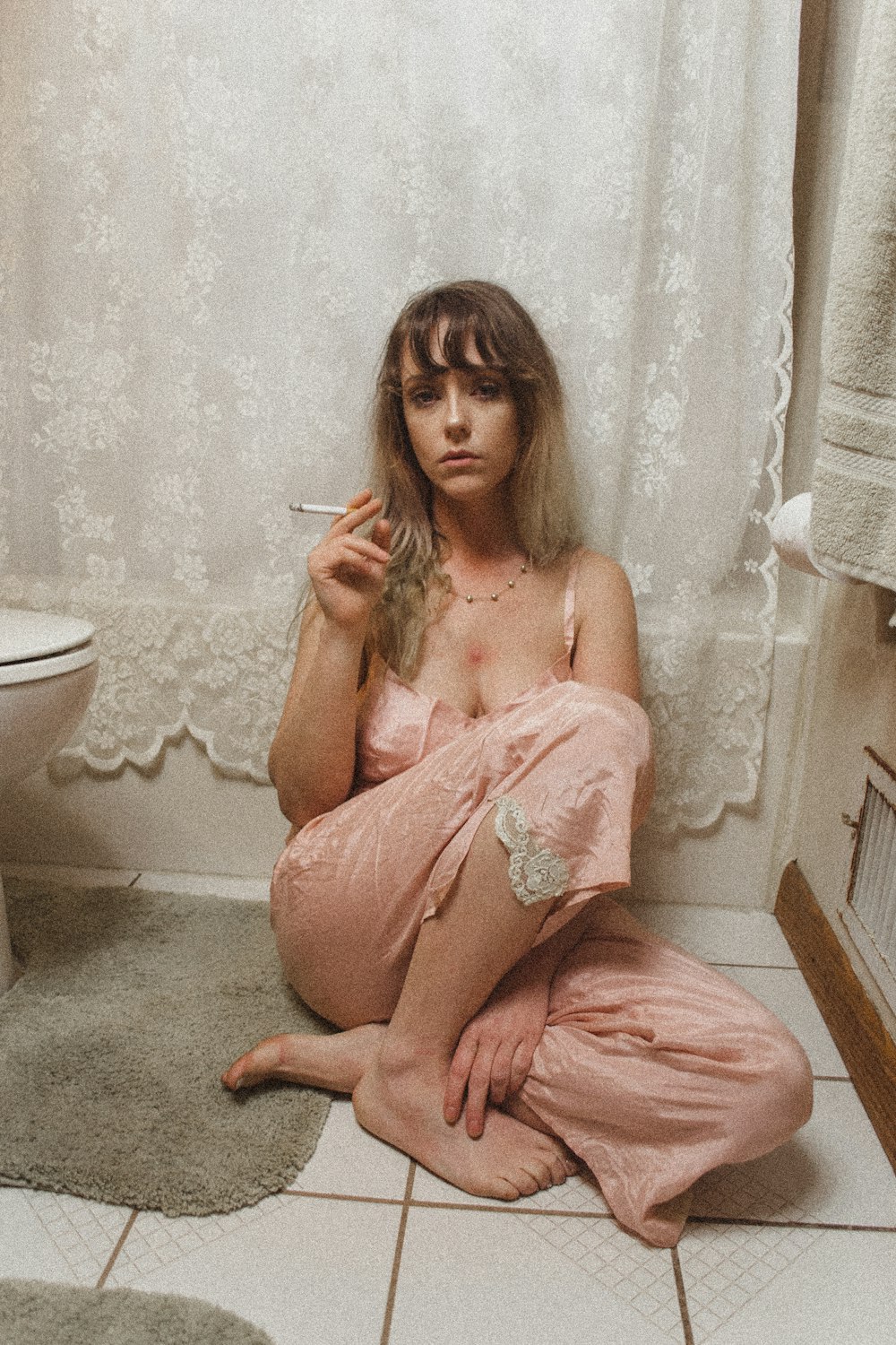 잠옷 바지를 입고 앉아 있는 여자가 화장실 안에서 담배를 피우고 있습니다