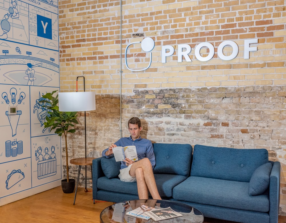 man sitting on blue sofa while reading book