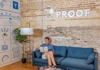 man sitting on blue sofa while reading book