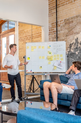 three men sitting while using laptops and watching man beside whiteboard