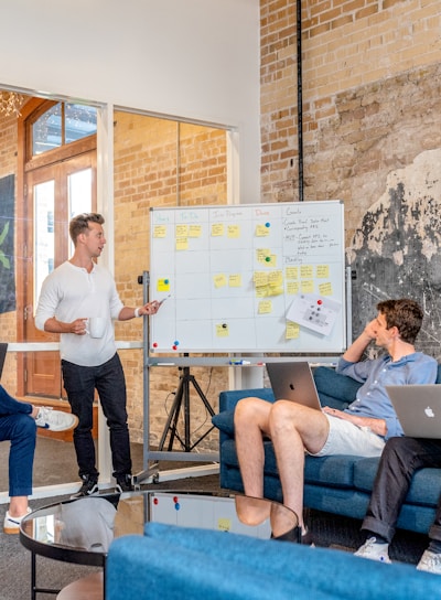 three men sitting while using laptops and watching man beside whiteboard