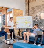 three men sitting while using laptops and watching man beside whiteboard