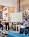 three men sitting while using laptops and watching man beside whiteboard