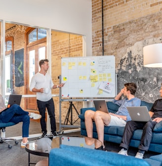 three men sitting while using laptops and watching man beside whiteboard