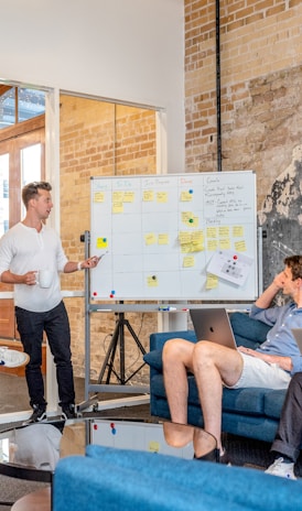 three men sitting while using laptops and watching man beside whiteboard