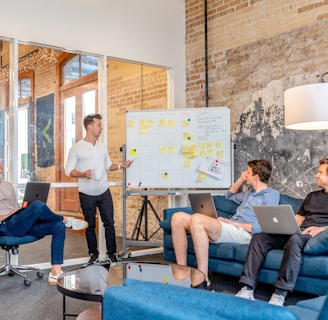 three men sitting while using laptops and watching man beside whiteboard