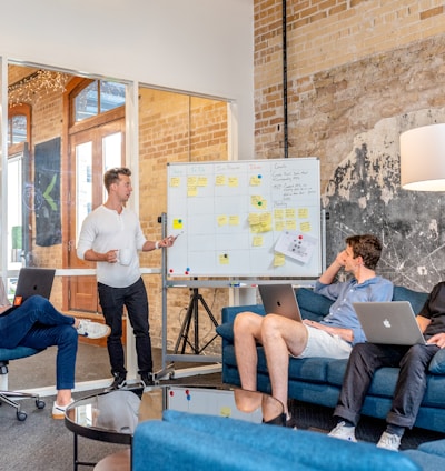 three men sitting while using laptops and watching man beside whiteboard