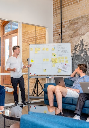 three men sitting while using laptops and watching man beside whiteboard