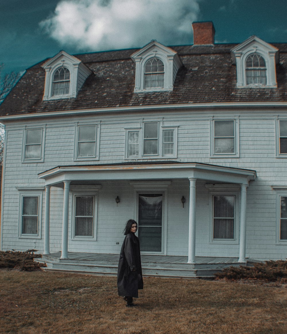 girl in gray jacket standing in front of white wooden house