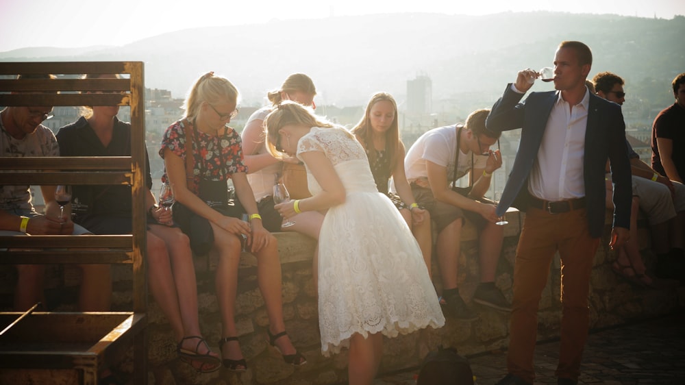 man drinking wine near woman and others are sitting sitting on railings