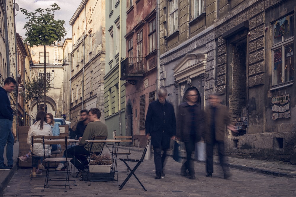 three men walking beside sitting people on alleyway during daytime