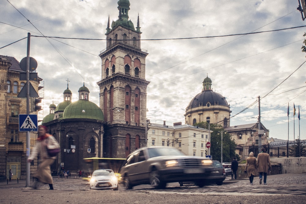 passing vehicles and walking people in front of brown concrete building under cloudy sky during daytime