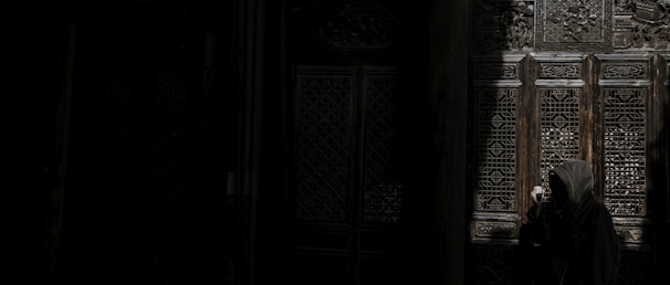 A mysterious figure wearing a hooded cloak, standing in front of a wall covered in cryptic runes.