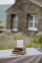 A rustic wooden table displaying an assortment of handmade candles and a stack of used novels.