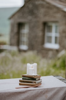 A rustic wooden table displaying an assortment of handmade candles and a stack of used novels.