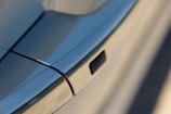 A close-up view of a car door handle with sleek, smooth metal surfaces and clean lines, reflecting a modern design. The handle appears to be flush with the car door, suggesting an aerodynamic and minimalist appearance.
