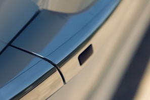 A close-up view of a car door handle with sleek, smooth metal surfaces and clean lines, reflecting a modern design. The handle appears to be flush with the car door, suggesting an aerodynamic and minimalist appearance.