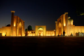 A peaceful evening view of the madrasa buildings with warm lights glowing inside.