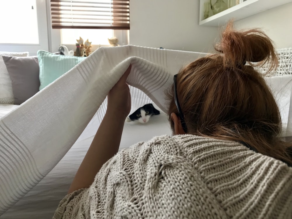 woman peeking cat covered with white blanket