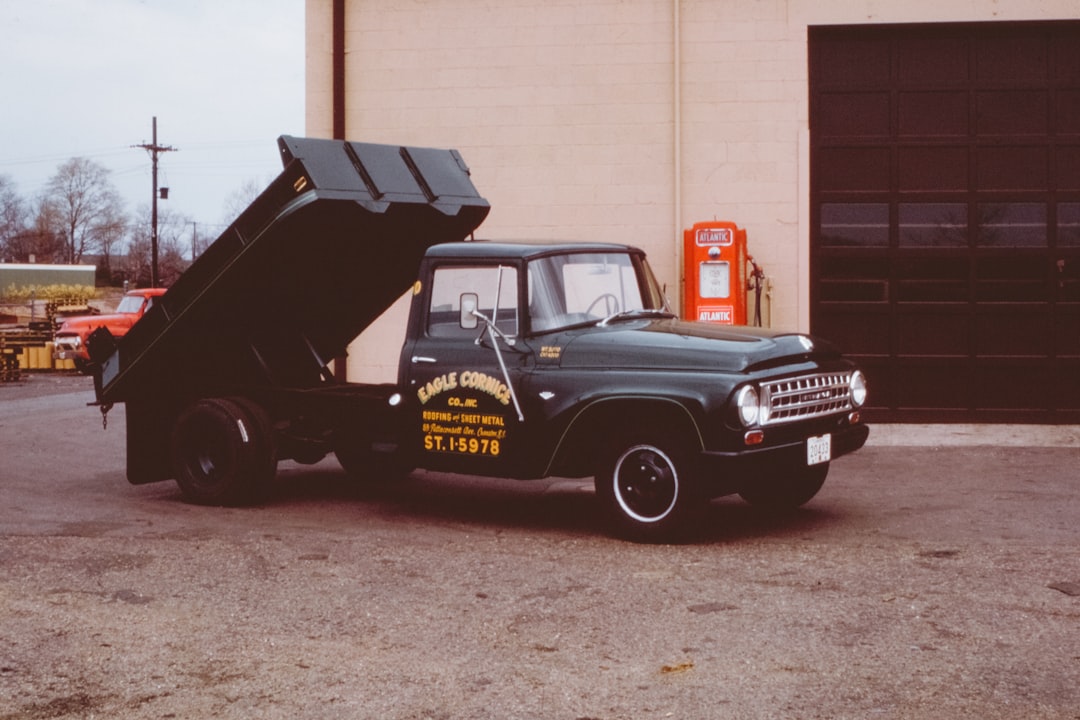 classic black single cab dump truck near building and gas dispenser