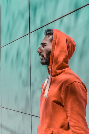 Close-up of a model wearing a deep navy hoodie with amber orange accents, standing against a gritty city wall.