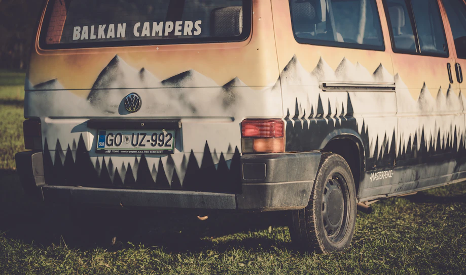 A sleek camper van outfitted with solar panels parked against a rugged mountain backdrop at sunset.