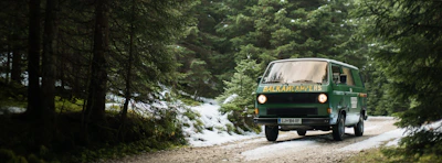 A rugged 4x4 campervan driving along a winding mountain road surrounded by deep green forests.