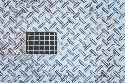 A metal surface with a diamond plate pattern, rusted and weathered, featuring a rectangular section with a different grid pattern.