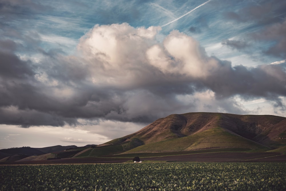 green field and mountain under cloudy sky