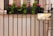 A metal fence with a rectangular brass plaque that reads '20 Essex Street' is set against a pale building. Bright red flowers and green foliage are seen in a planter box atop the fence, adding color and life to the scene.