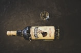 A bottle of Cabrito Reposado tequila lies horizontally on a dark textured surface. There is a small glass filled with a clear liquid positioned near the bottle.