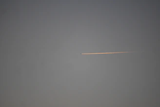 An aerial shot capturing a jet trail cutting sharply across a bright, clear sky.