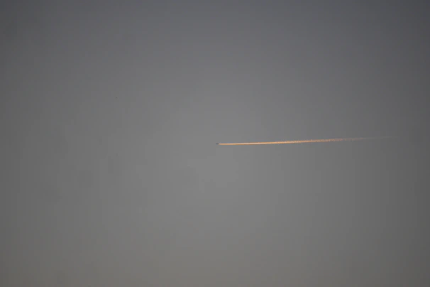 An aerial shot capturing a jet trail cutting sharply across a bright, clear sky.