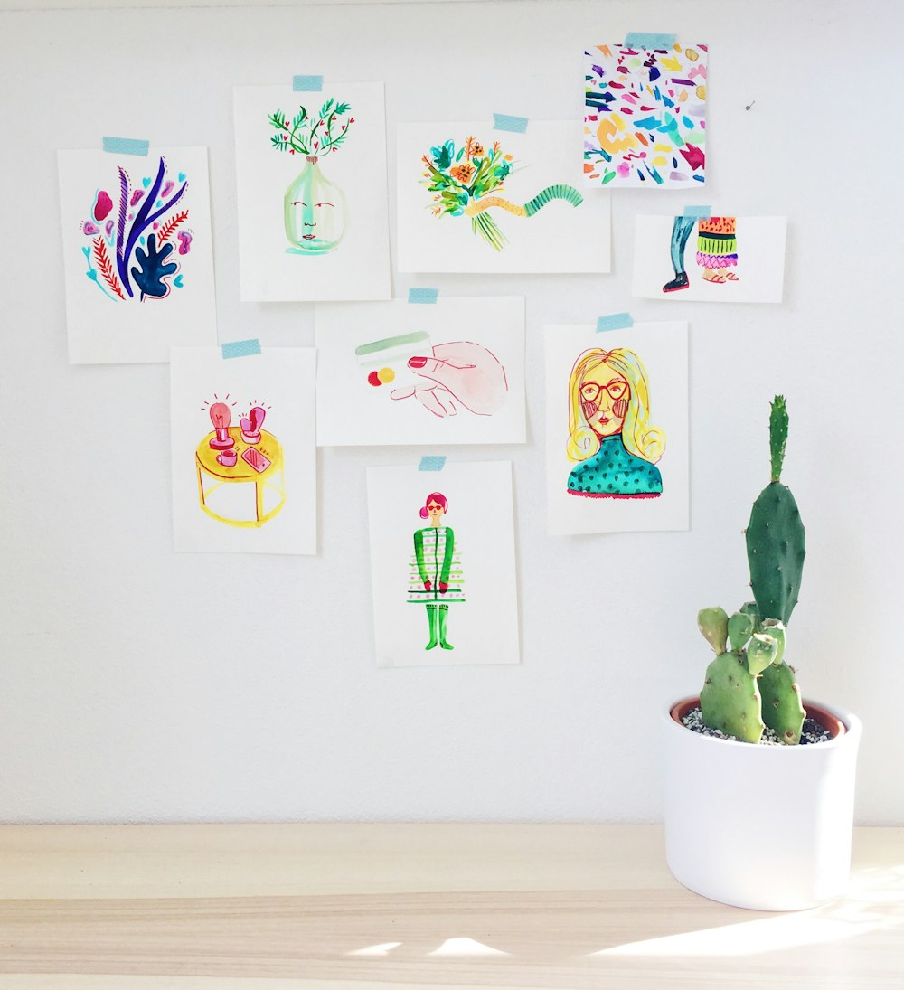 Abstrakte Gemälde in verschiedenen Farben an der Wand in der Nähe einer grünen Kaktuspflanze im weißen Topf