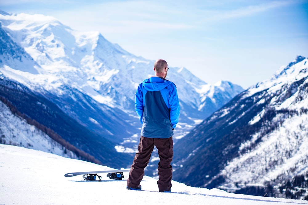 man wearing blue jacket standing on snow covered mountain