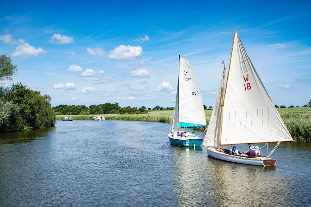 two white sailboats on river under white clouds